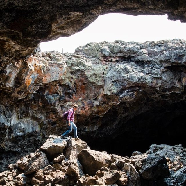 A visitor stands inside a lava tube, under a large opening to the surface