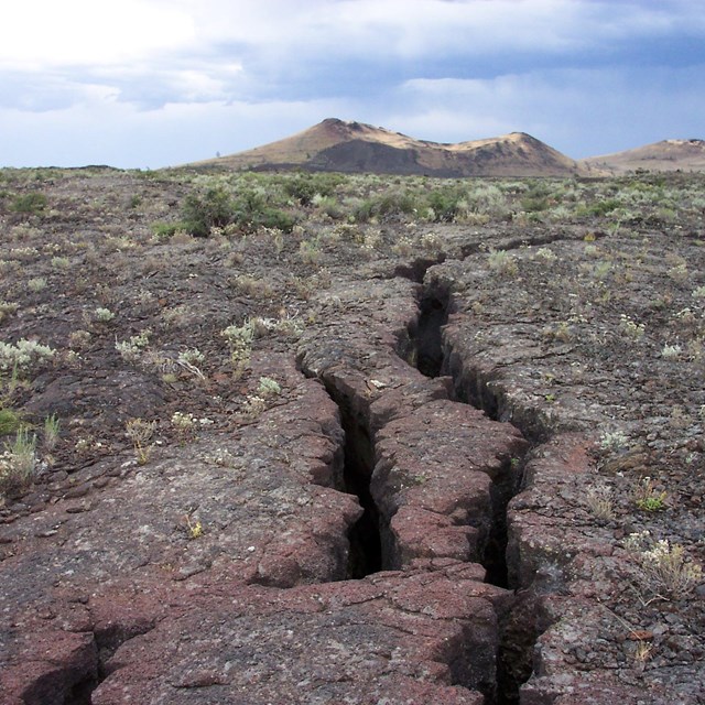 two deep cracks several inches wide extend toward distant cinder cones