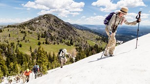 Hikers climbing snow-covered section of a mountain using ski poles
