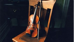 Violin resting on back of chair in darkened room