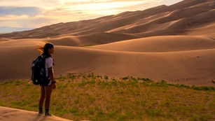 Kid with a backpack standing near sand dunes at dusk