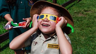 Kid wearing a park ranger costume wearing filtered glasses while looking up