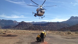 Two people below a helicopter making its landing approach