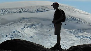 Hiker standing with pack on and snowy mountains in the distance.