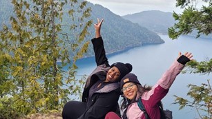 Two hikers near water holding their hands up in triumph 