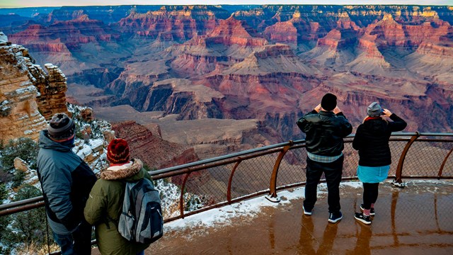 A few visitors standing on an overlook of a snow-dusted canyon