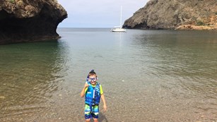 Kid in snorkel gear staking in a cove