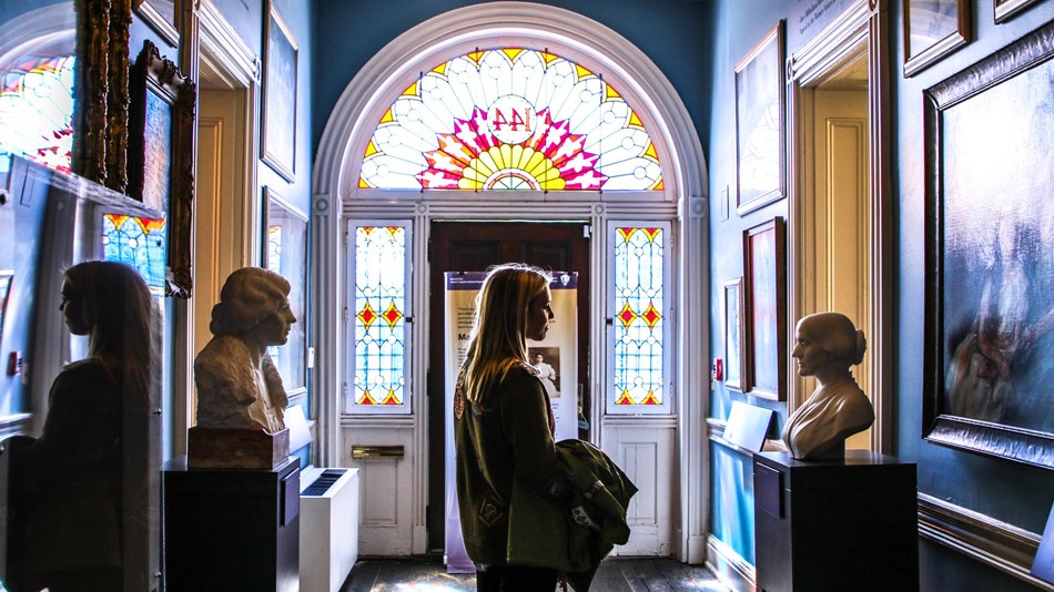 Woman looking at statues in front of stained glass windows in hallway