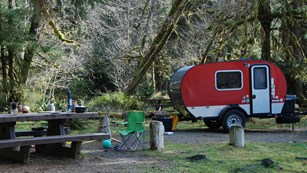 Red camper parked near a picnic table. 