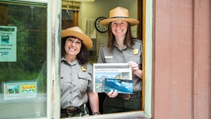 Two rangers standing in an entrance station window holding park brochures