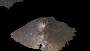 Siloutte of a photographer standing under a geological arch with a star-filled sky in the background