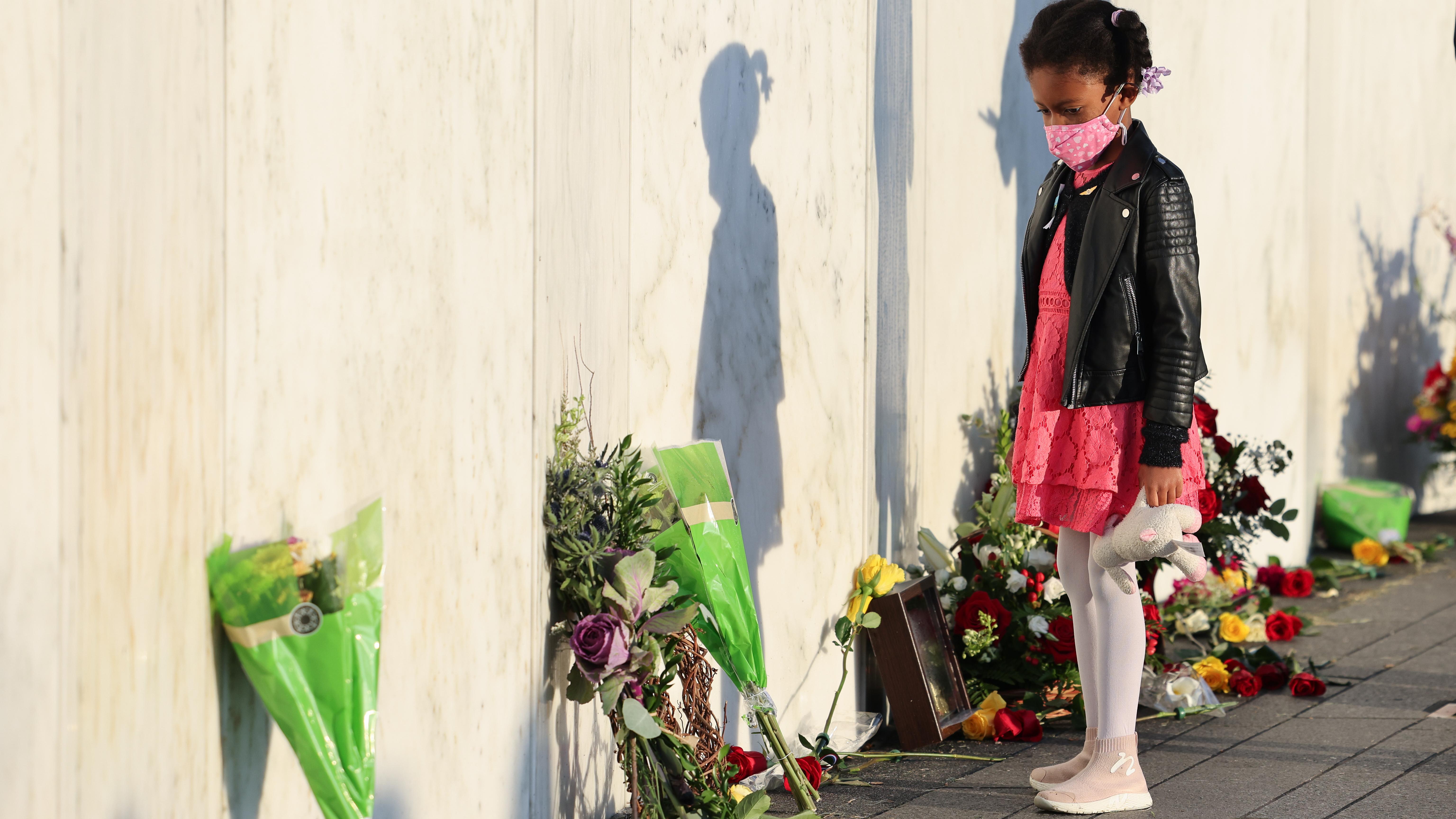 A child at a memorial wall decorated with flowers