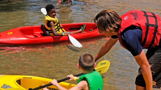Woman helping two young children in kayaks
