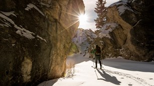 Skiier passing tall snow-covered rock faces