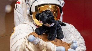 Astronaut holding a small black plush dog