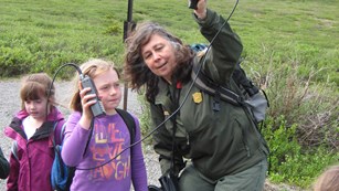 a ranger holds up a radio tracking tool while talking to children