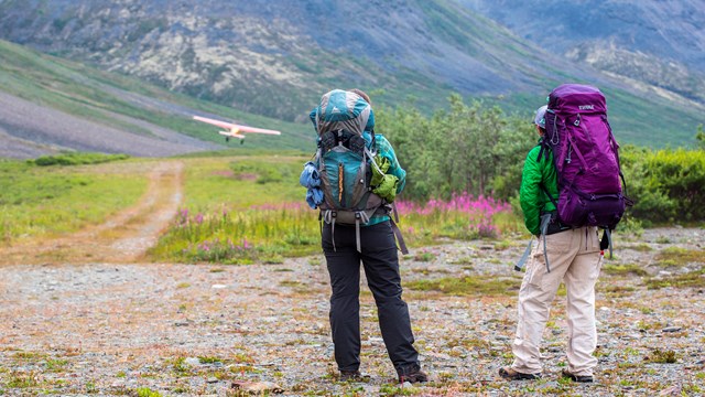 Two backpackers in a mountain valley watching their plane leave