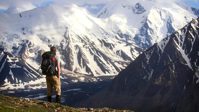 Backpacker facing away looking out over snow-capped mountains