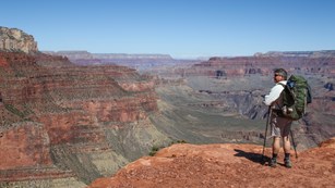 Visitor with a full backpack and walking sticks standing over the Grand Canyon