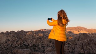 Visitor taking a picture of a desert canyon at sunset
