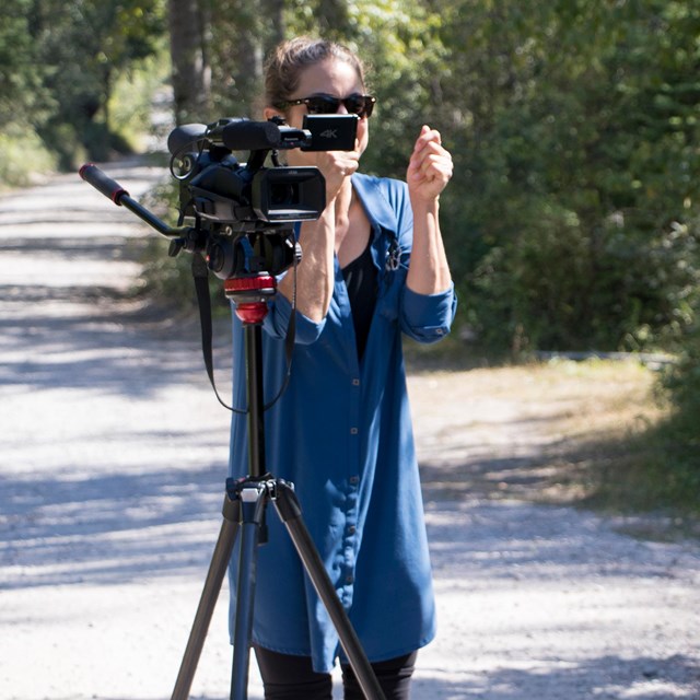 A young woman stands behind a video camera.