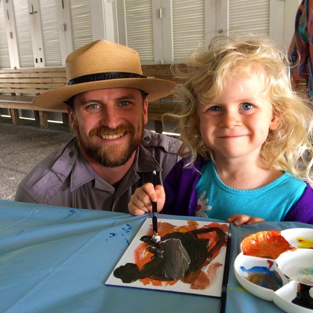 Ranger and little girl work on painting an art project
