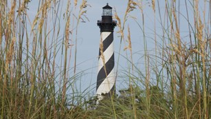 The black and white spiral stripes of the Cape Hatteras Light Tower behind a sand dune with oats