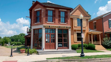 Two story shop on a brick road with pane windows and a sign saying