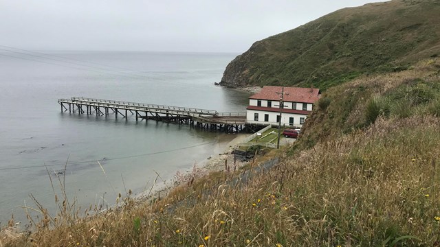 View from atop an exposed bluff includes an overcast bay, Point Reyes Life Saving Station, and wharf