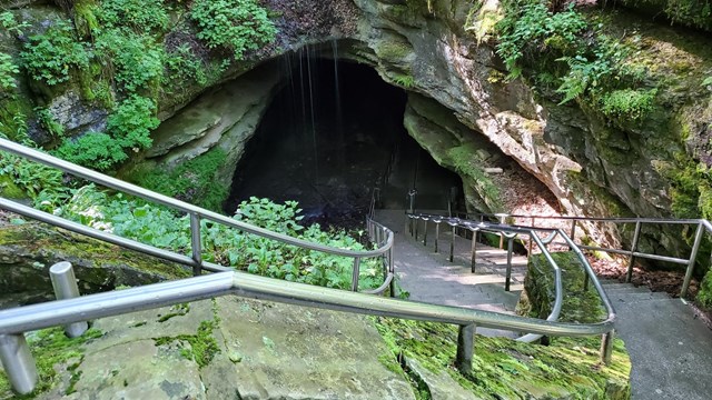 A double staircase with a metal railing on the sides and middle leads into a rocky cave entrance.
