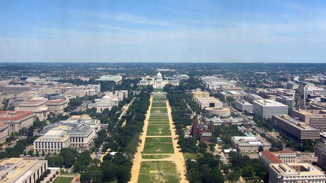 Aerial view of worn turf on the National Mall, surrounded by buildings and trees 