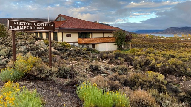 A visitor center building on a brushy hillside with a sign pointing to Visitor Center and Campground