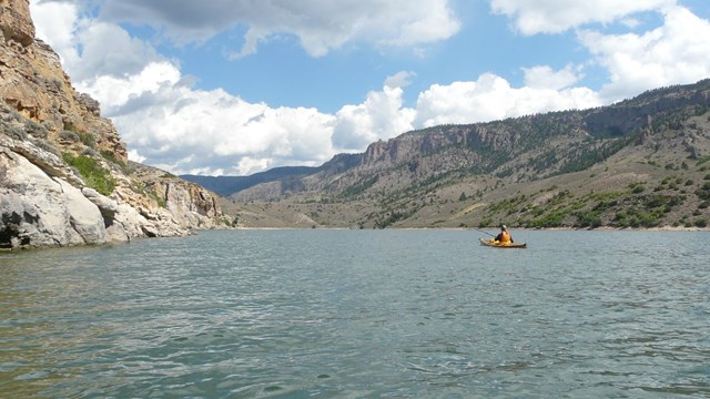 A yellow kayak in a large body of water between mesa walls
