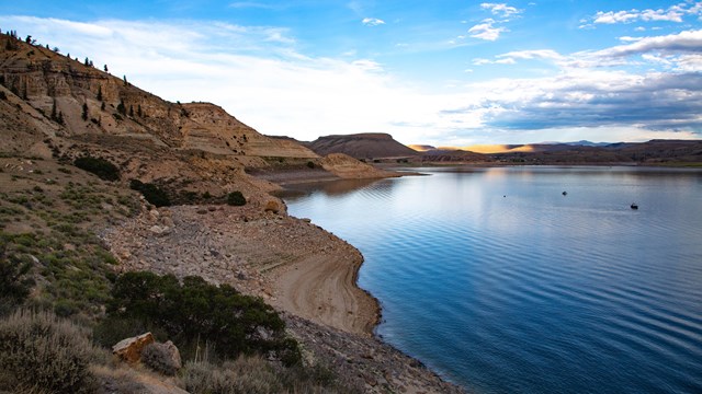 A blue reservoir with mesas surrounding it and a small boat on the water