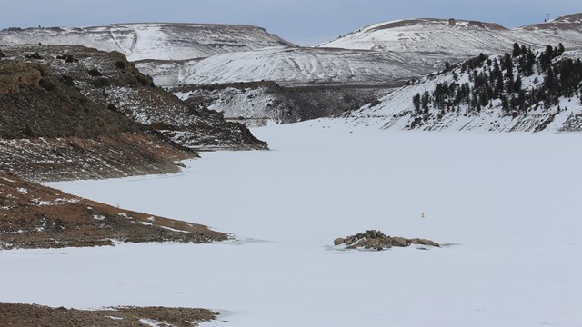A snowy landscape surrounded by rocky cliffs and sparse trees.