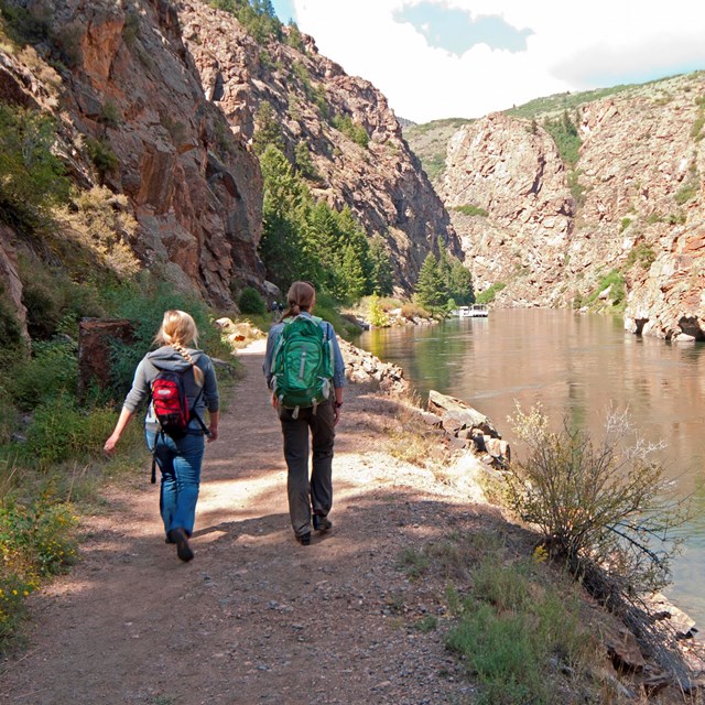 A photo of two people hiking on a path along a waterway