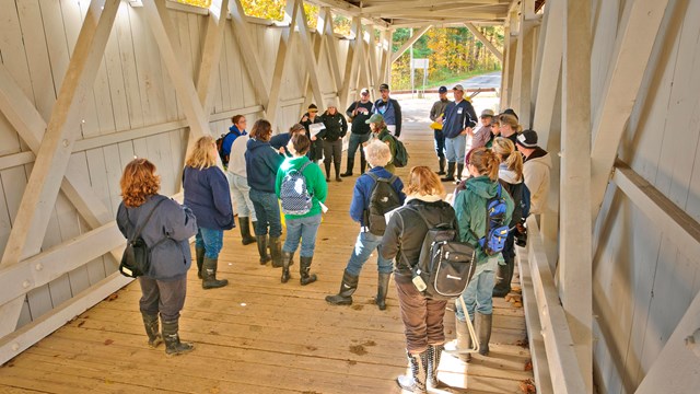 A group of educators stands inside the Everett Covered Bridge, listening to a ranger