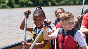 Two children in a boat holding oars. One is a black girl and one white boy, both about 8 years old.