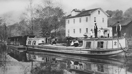 Black and white photo of a family standing and sitting on a white canal boat on the water.