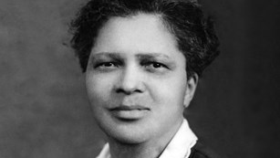 African-American woman with short hair, in a buttoned top with pleated front and a white collar.