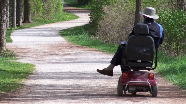 a park visitor enjoys the towpath trail from his motorized wheelchair, surrounded by trees