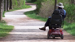 a park visitor enjoys the towpath trail from his motorized wheelchair, surrounded by trees