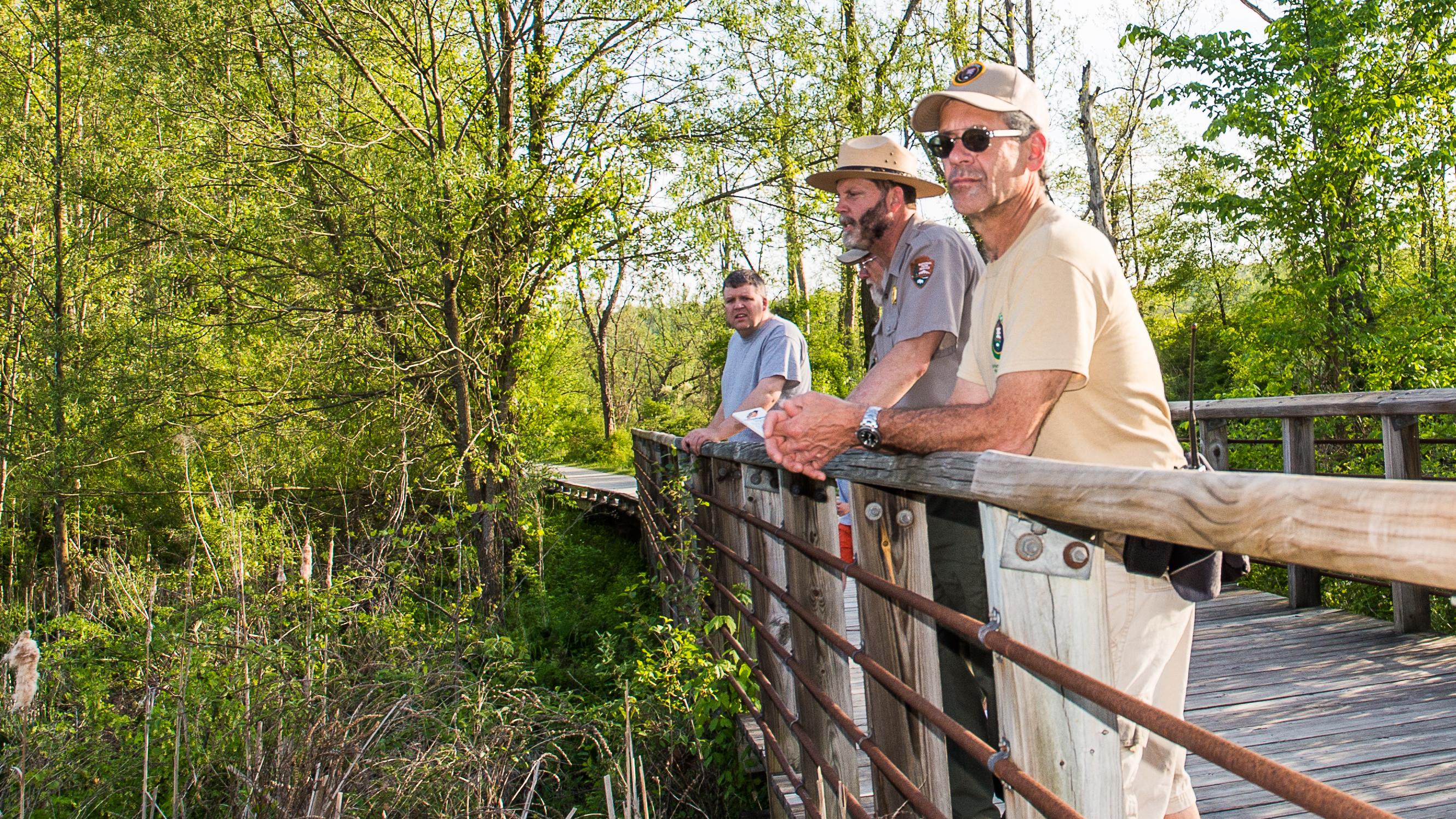 park visitors lean on a wood railing overlooking a pond