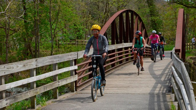 Three people wearing helmets bike over a bridge.