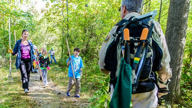 A woman and child walk down a trail towards a volunteer with trail maintenance equipment.