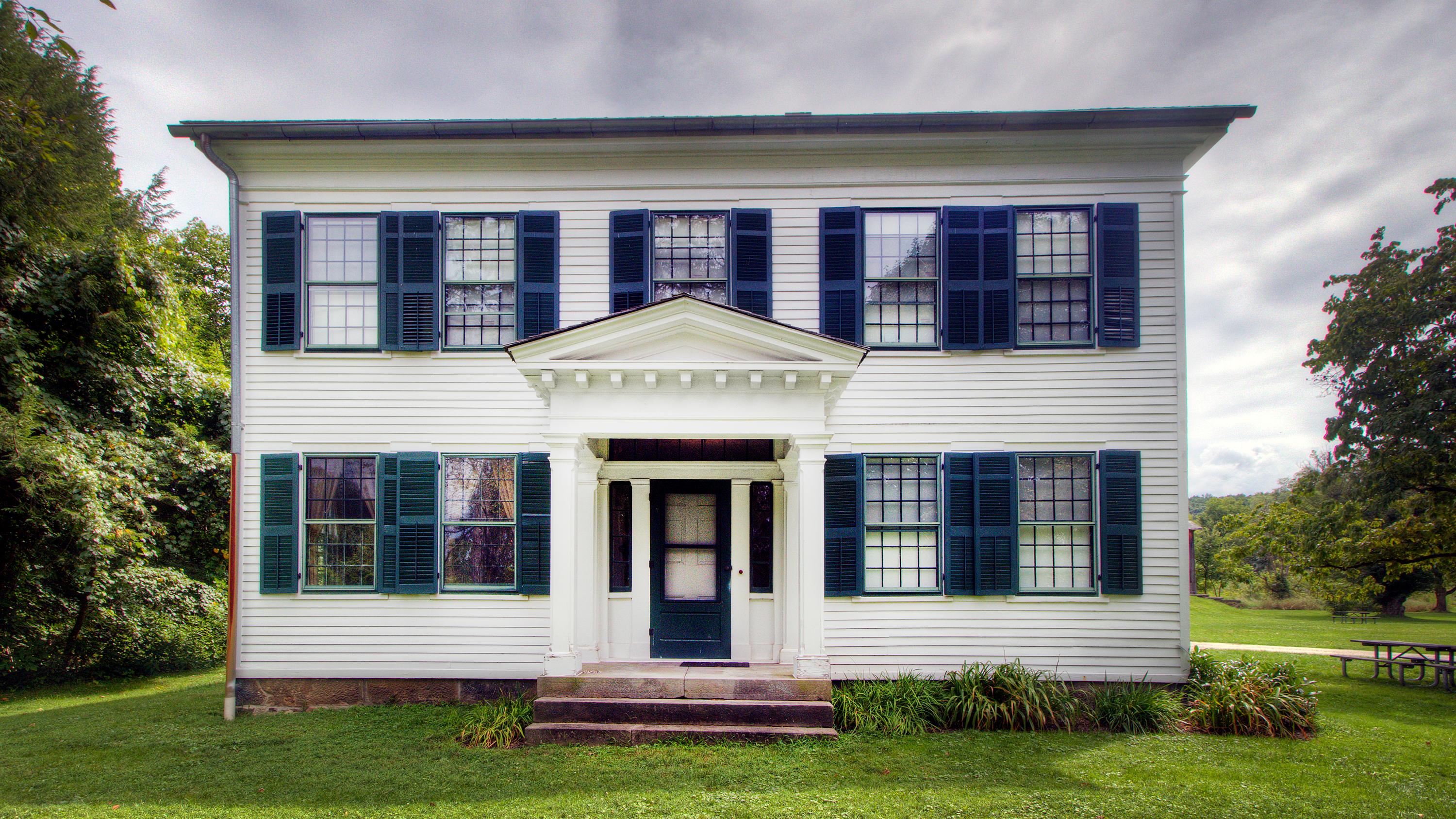 White, two-story building with two rows of windows with green shutters.