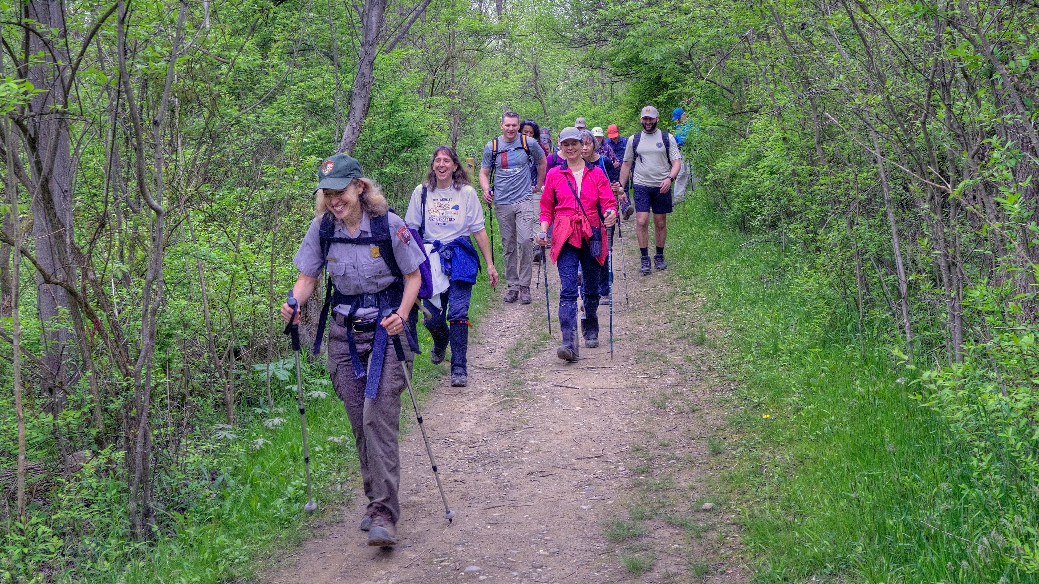Uniformed ranger leads a group of hikers down a trail through the forest.