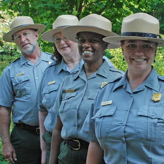 Four rangers is uniforms and flat hats stand in a diagonal line facing the camera.
