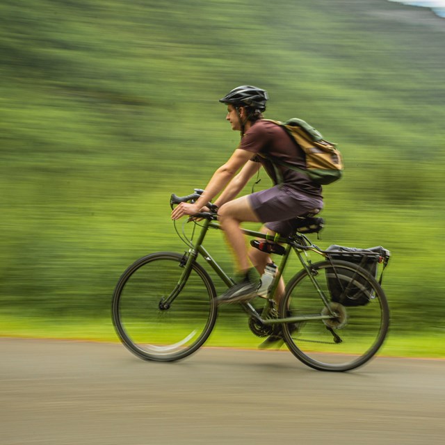 A person wearing a helmet and backpack rides a bicycle.