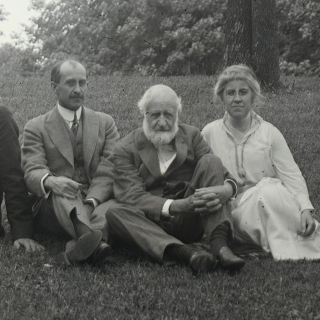 Seven people sitting on a hillside in front of a large home